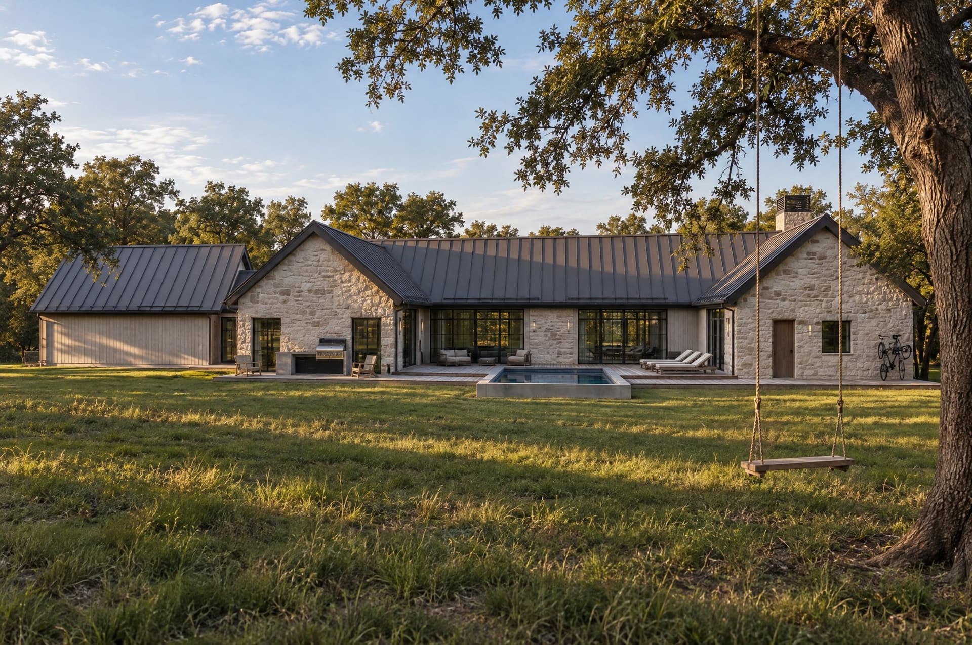 A long limestone house with a metal roof, a pool, and a rope swing under an oak.