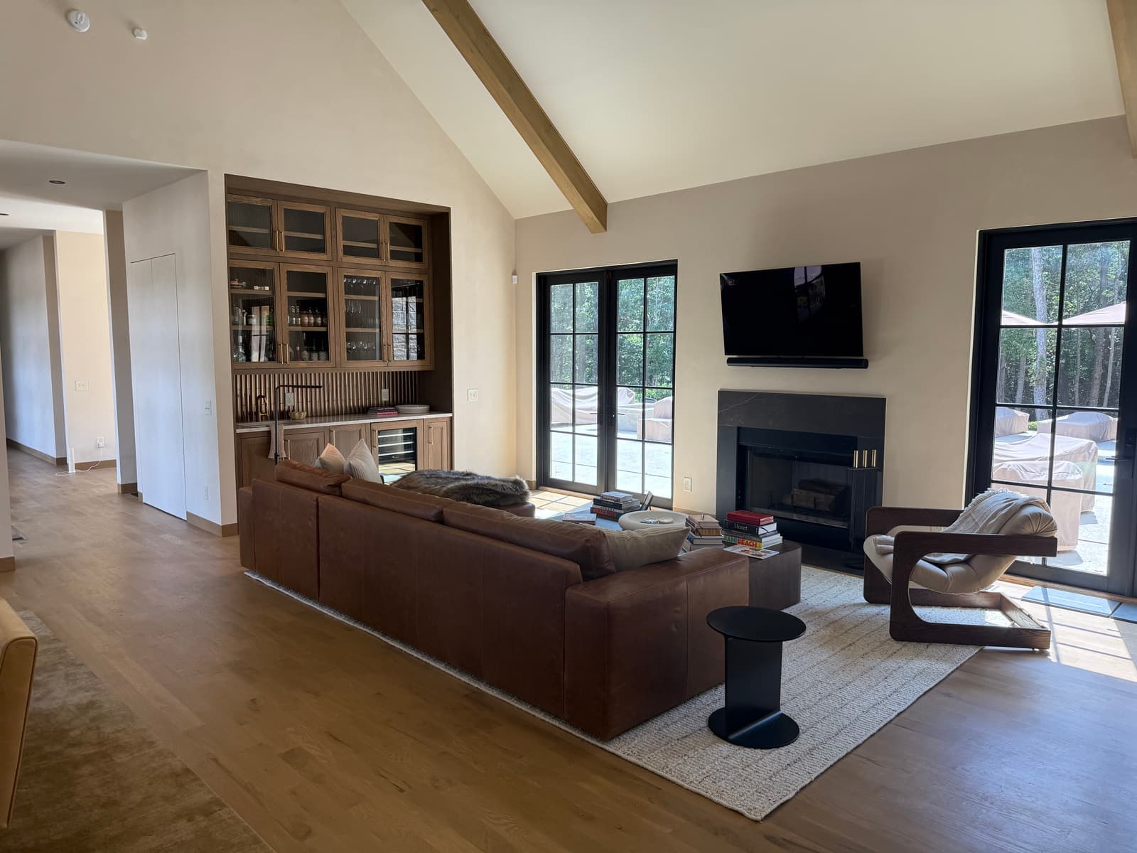 A living room with a vaulted ceiling, wood beams, and tall windows.