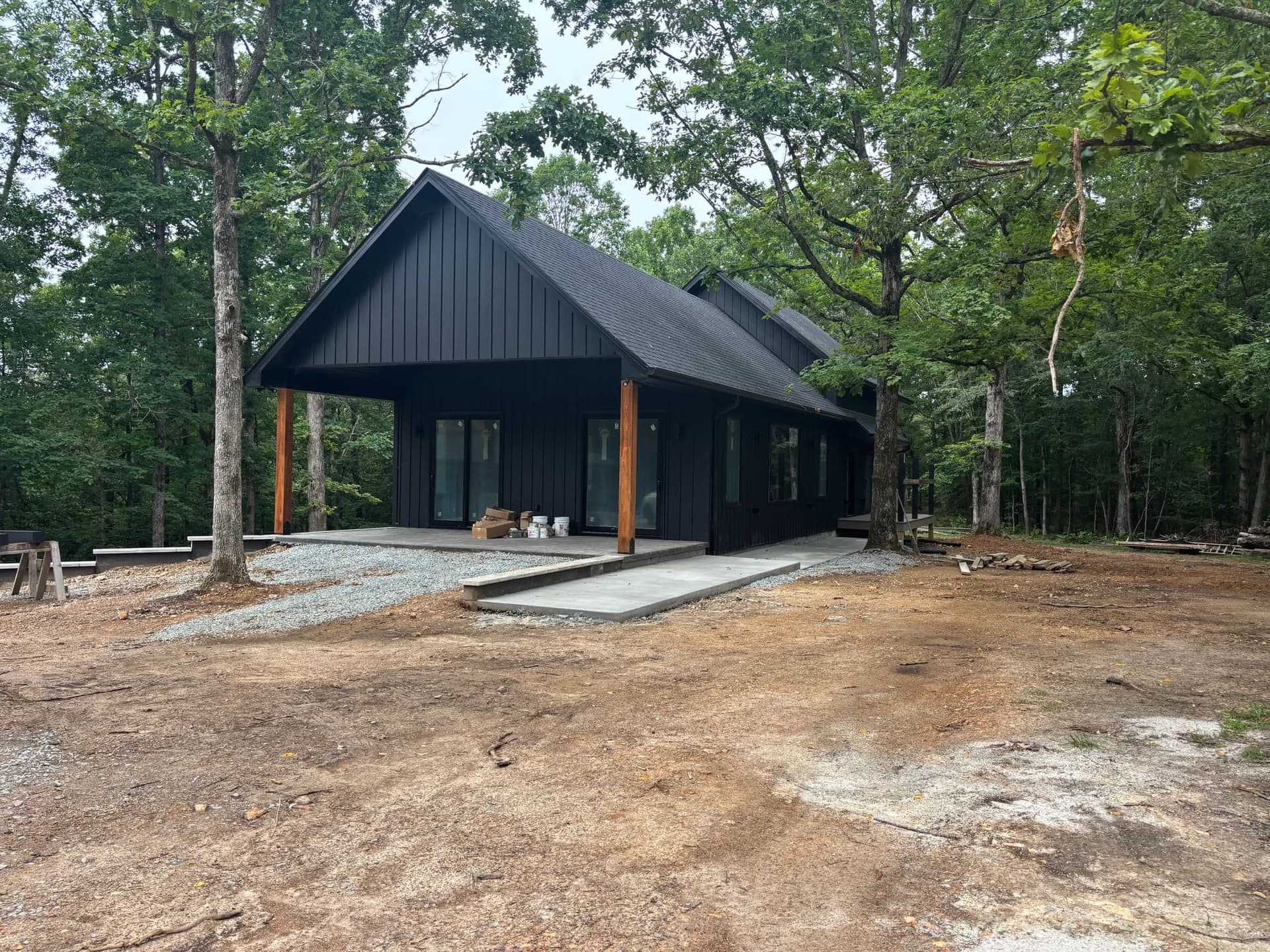 A black gabled house under hardwoods, the ground around it still open.