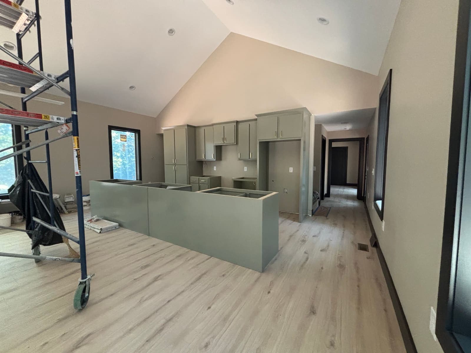 The kitchen during fit-out: sage cabinets, island carcass, scaffold at the left.