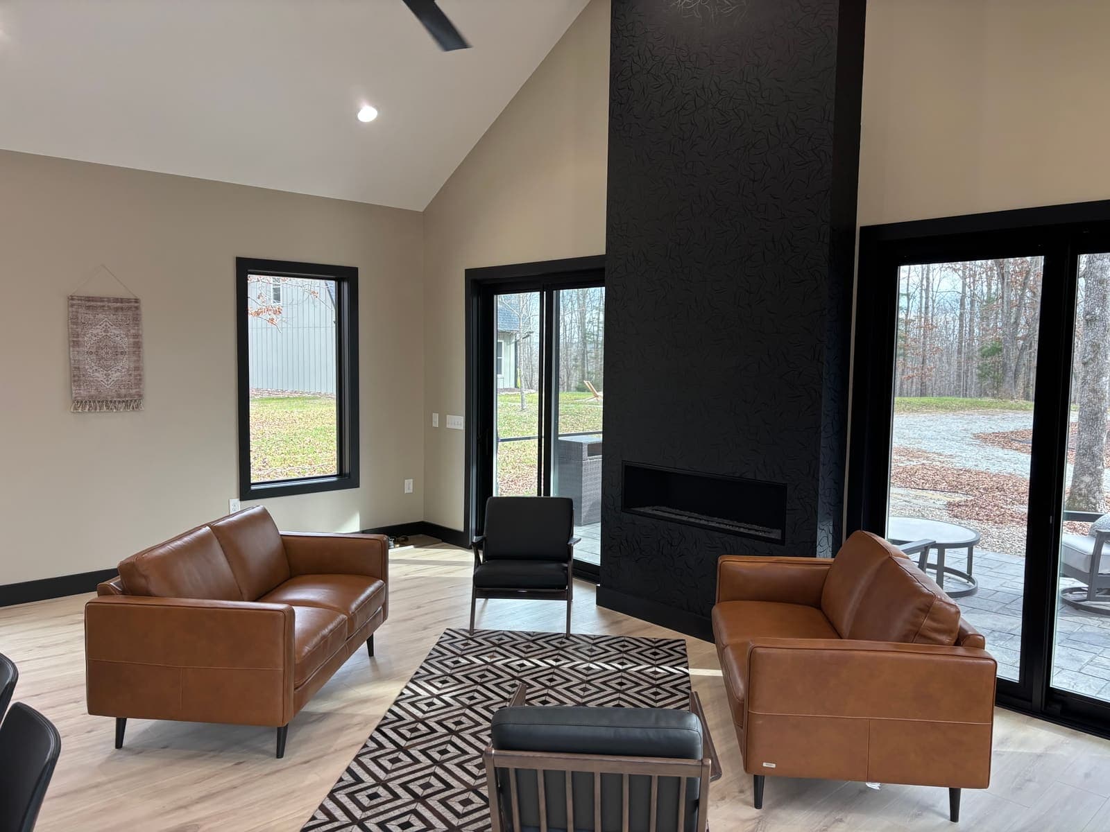 Leather sofas facing a black fireplace, doors open to the trees.