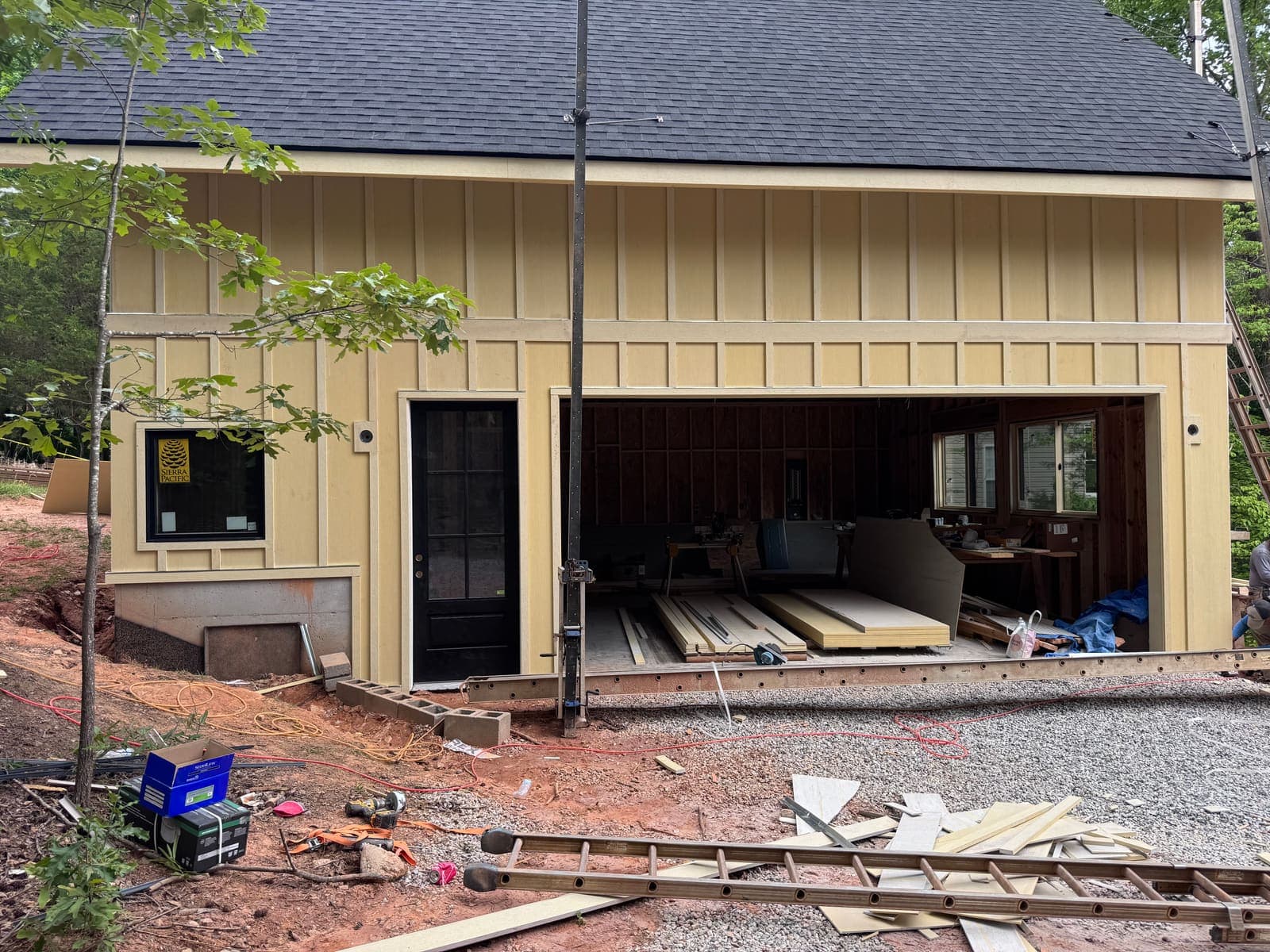 Tan board-and-batten, a black door, and the garage bay still open.