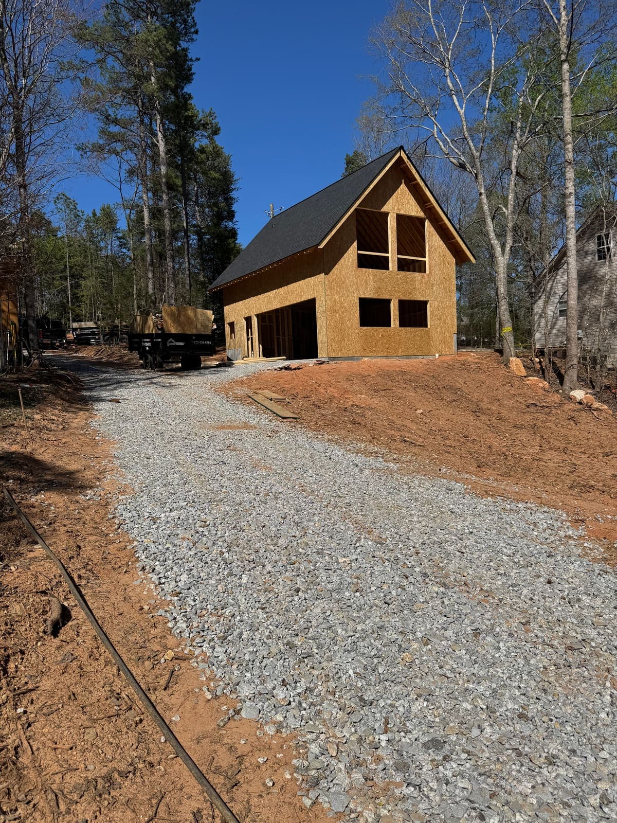 The sheathed gable at the end of a gravel drive, red soil on either side.