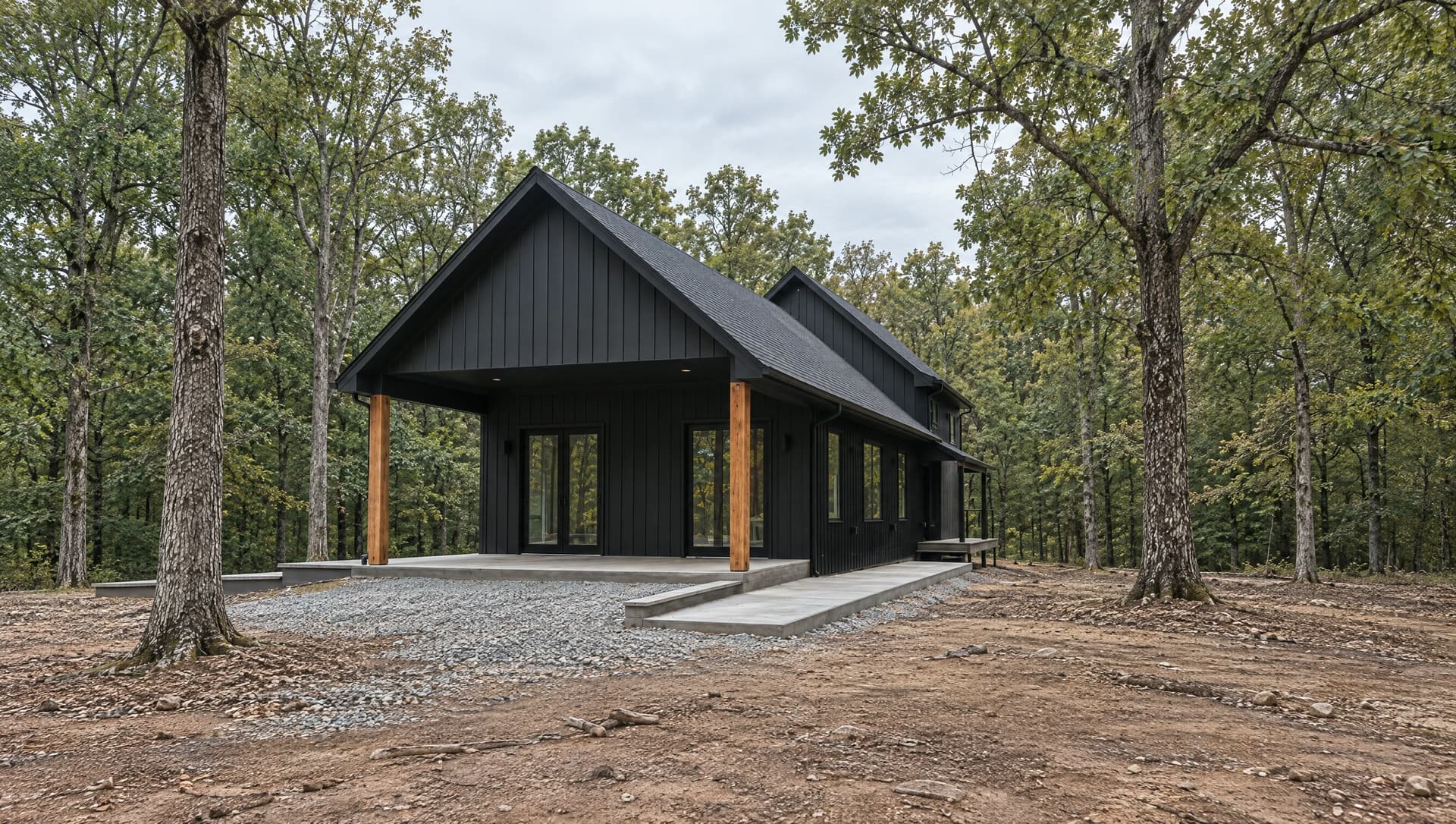 A black gabled house among oaks, with gravel and an open yard.