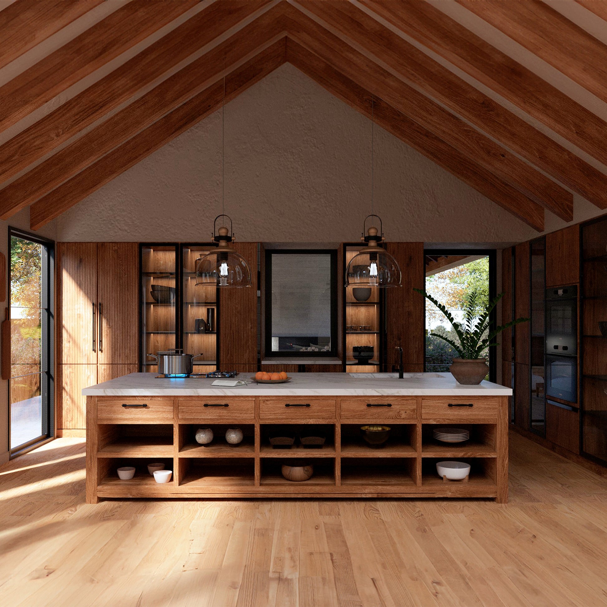 A spacious kitchen with a vaulted wooden ceiling and exposed beams. The room features a large wooden island with open shelves, a white marble countertop, and two glass pendant lights hanging above. The back wall has built-in wooden cabinets with glass doors, black metal hardware, and a central window. Natural light streams through large glass doors on both sides, revealing greenery outside