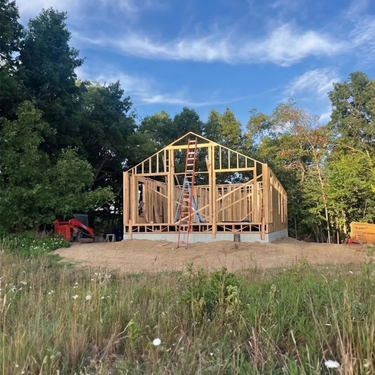 Wooden house frame under construction with trees and blue sky in the background