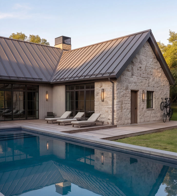 The Cedar Residence - Modern single-story house with a stone exterior, dark metal roof, large glass windows, a wooden deck, three outdoor lounge chairs, and a swimming pool in the foreground.
