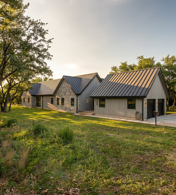 The Cedar Residence - A modern rustic cabin complex with gray siding and dark metal roofs, set in a grassy field with trees under a warm sky.
