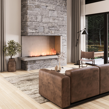 Modern rustic living room with a floor-to-ceiling stone fireplace, cozy fire, and natural wood flooring. A brown leather sofa sits on a textured rug facing a round white coffee table. Large glass doors and tall vertical slat windows flood the space with natural light and offer views of a landscaped yard and surrounding greenery.