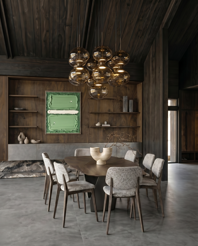 Casa del Prado - A modern dining room with a dark wood ceiling and built-in shelving, featuring a round wooden dining table surrounded by upholstered chairs. A large cluster chandelier hangs above, and a green framed artwork is mounted on the wall.