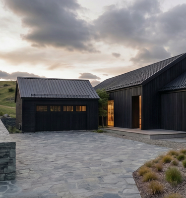 Casa del Prado - Modern black wood chalet with a stone paved driveway and landscaped grounds under a dramatic cloudy sky.