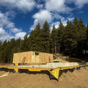 Building site with wooden frame structure against a blue sky with clouds and trees.