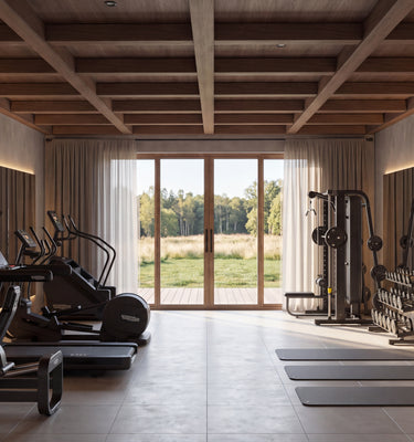 The Hunters Lodge: A spacious indoor gym with exercise equipment including treadmills, weight machines, a hanging punching bag, and yoga mats, set in a modern room with large windows overlooking a grassy field.