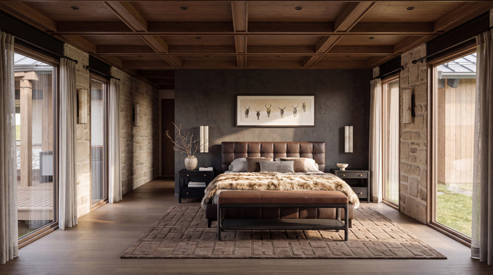 The Hunters Lodge: A luxury bedroom interior featuring a bed with a tufted headboard, patterned bedding, a matching bench, a textured area rug, a dark gray accent wall with framed art, and a rustic wood and stone ceiling.