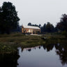 Front facade of nordic cabin design surrounding by trees on an open land near a pond