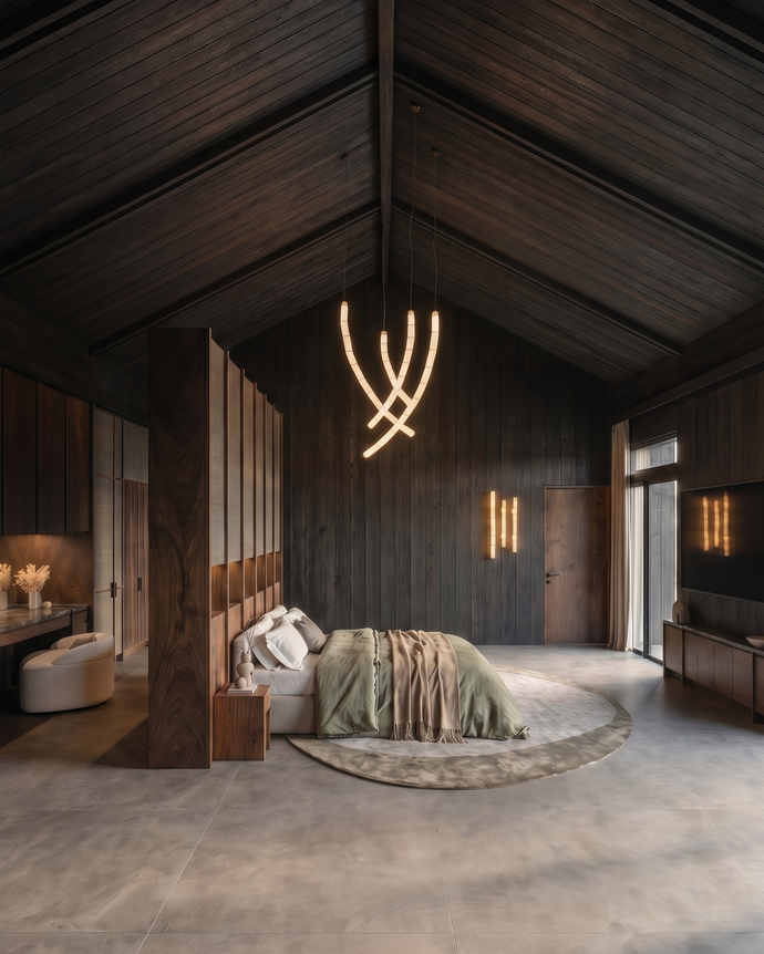 Casa del Prado - A luxury modern bedroom featuring a large bed with sage green and beige bedding, set in a spacious room with dark wood-paneled walls and ceiling, a circular concrete floor, and a sculptural illuminated pendant light.