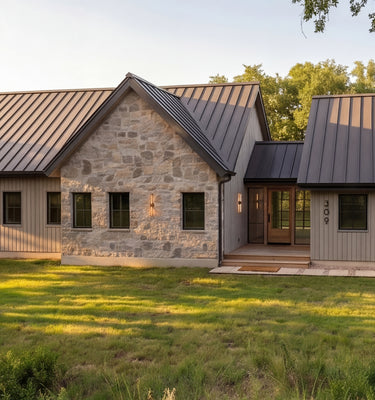 The Cedar Residence - A modern farmhouse-style house exterior featuring a stone facade on one section, horizontal siding on others, a dark metal roof, and a grassy lawn in the foreground.