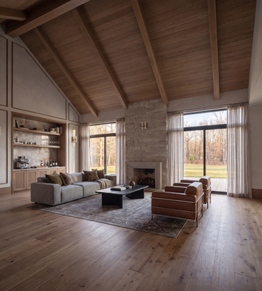 Coyotes Den: A high-ceilinged rustic living room with a wood-paneled vaulted ceiling, stone fireplace, hardwood floors, a light gray sofa, two brown leather armchairs, and large windows with sheer curtains.