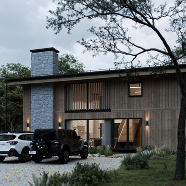 Modern two-story cabin with vertical wood siding and a large stone chimney, viewed from a gravel driveway with two parked SUVs. Warm interior lighting reveals a staircase and dining area through expansive glass windows. Surrounded by trees and landscaped greenery, the home blends rustic charm with contemporary design.